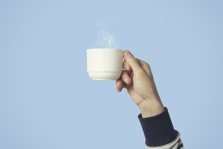 Male hand holding a white cup with hot coffee or tea on a light blue background. Breakfast concept with hot coffee or tea.の写真素材