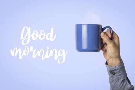Male Hand is holding a blue cup with hot coffee or tea on a blue background. Added text Good morning. Breakfast concept with hot coffee.の写真素材