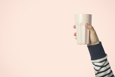 Male hand holding a purple cup with hot coffee or tea on a light pink background. Breakfast concept with hot coffee or tea.の写真素材