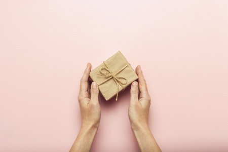 Female hands holding a gift box on a pink background with a question mark. Surprise concept, waiting for a gift for the holidays, birthday, christmas, wedding. Flat lay, top view.の写真素材