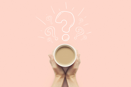 A hand is holding a cup with hot coffee on a pink background. Question mark. Breakfast concept with coffee or tea. Good morning, night, insomnia. Flat lay, top view.の写真素材