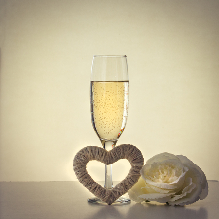 A glass with champagne, a white rose and a heart of handmade.の写真素材