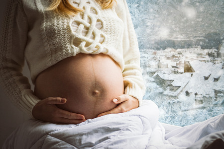 Pregnant young girl near the window in a frosty day.の写真素材