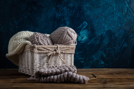 Light gray Knits in a basket and knitting needles, a white knitted scarf on a dark blue background. The concept of handmade.の写真素材