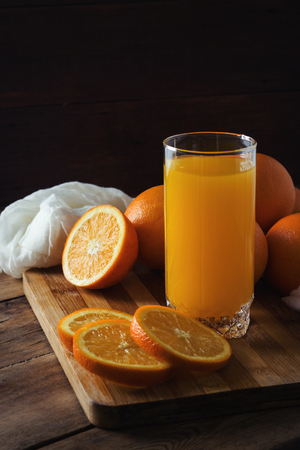 A glass of orange juice, a sliced orange, oranges on a wooden board, a dark background. Beautiful Game of Light and Shadows.の写真素材