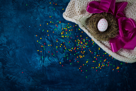 Easter Egg in a nest, pink ribbon, white scarf and pastry decorations on a blue background. The concept of Easter. Copy space. Flat lay, top view.の写真素材