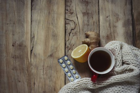Ð¡up of hot tea, lemon, ginger, tablets and a white torn scarf on a wooden background. Top view,flat lay. Cold treatment.の写真素材