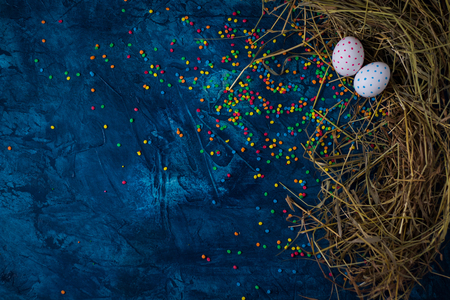 Two Easter Eggs and straw around, colored sweetness decorations on the Blue Background. Added a flare effect. Copy space. Flat lay, top view.の写真素材