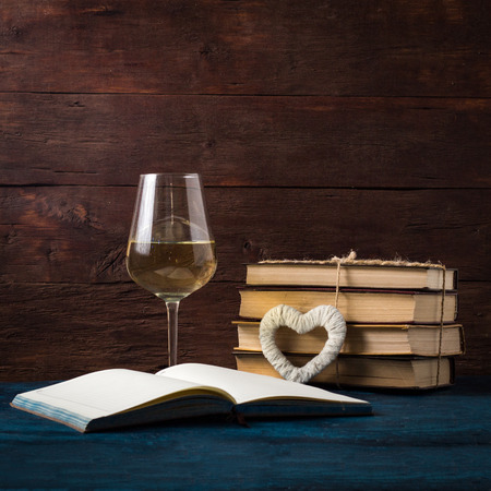 Glass with White Wine, Open Book, White Heart on the Blue Table.の写真素材