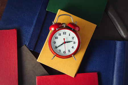 Red Alarm Clock and Deployed Books on the Dark Wooden Background. top view.の写真素材