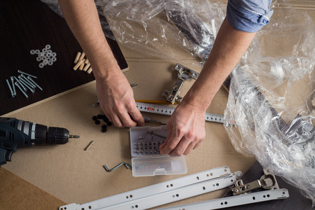 Hands of a man with a tool. Screwdriver, Screws, Furniture Details. Concept Workshop. Flat lay, top...