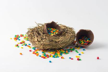 Broken Chocolate Easter egg with multi-colored candy decorations in the nest on a white background. Easter concept.の写真素材