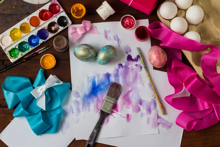 Preprimary painting of Easter Eggs, Brushes, Paints, Eggs, Sweets, Ribbons on the Dark Wooden Table. The concept of Easter. Flat lay, top view.の写真素材