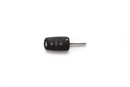 Black key ring with car key with remote control over white background.