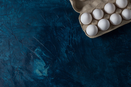 White Eggs in an open cardboard box on a blue background. The concept of Easter. Natural healthy...