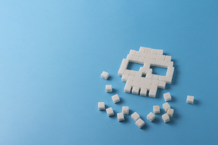 Skull of cubes of sugar and pieces of sugar on a blue background. Concept Sugar kills and harm sweet on the human bodyの写真素材