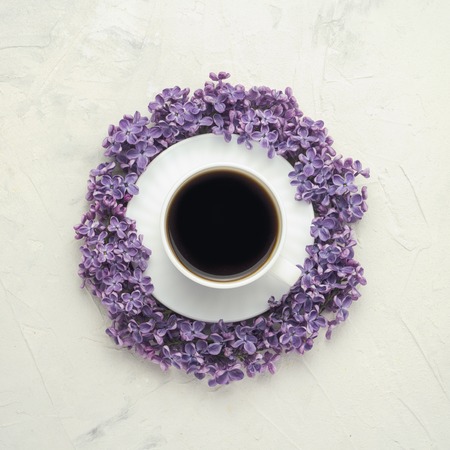 A cup with a coffee on a saucer, surrounded by lilac flowers on a white background. Top view, flat, lay, copy spaceの写真素材