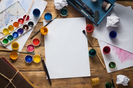 The Artist's Workplace with Watercolor Paint, Gouache, Brushes and Paper Sheets on a Wooden...
