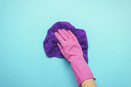 Female hand with pink gloves, holding a napkin to remove dirt and dust on a blue background....
