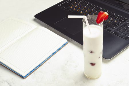 Workplace. On the table, a laptop, a diary and a milkshake with strawberries. Top view, flat layの写真素材