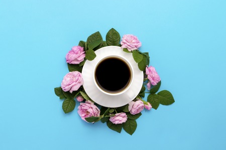 White cup with black coffee and pink roses lined around on a blue background. Flat lay, top view.の写真素材