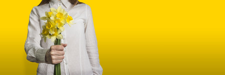 Young girl in white shirt with bouquet of flowers of narcissus in hand on yellow background.の写真素材