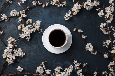 White cup with coffee and cherry branches with spring flowers on a dark blue background.の写真素材