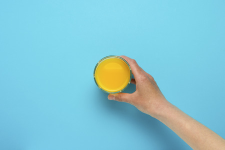 Female hand taking orange juice on a blue background. Flat Lay Still Life Table Top View Blue Background.の写真素材
