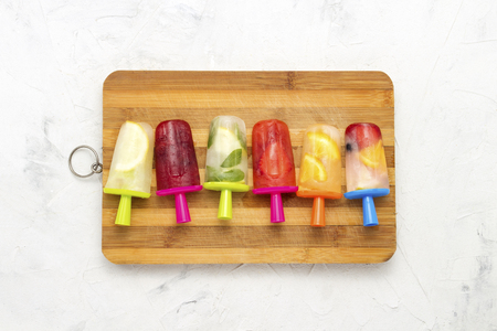Homemade colorful fruity ice creams on a wooden board and against a white stone background. Strawberry, Lemon, Lemon with mint, Orange, Cherry, Multifruit. Flat lay, top view.の写真素材