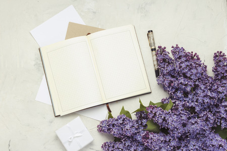 Open diary, pen, gift box, envelopes and a twig of lilac on a white stone background. Flat lay, top view.の写真素材