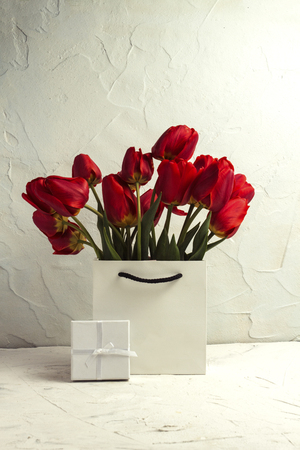 White Gift Bag, small white gift box, petals and bouquet of red tulips on a light stone background. Concept Offer a gift or an engagement, marriage.の写真素材