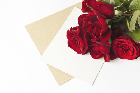 Bouquet of red roses and an envelope with a note on a white background. Concept of a romantic gift for a loved one. Wedding themes.の写真素材