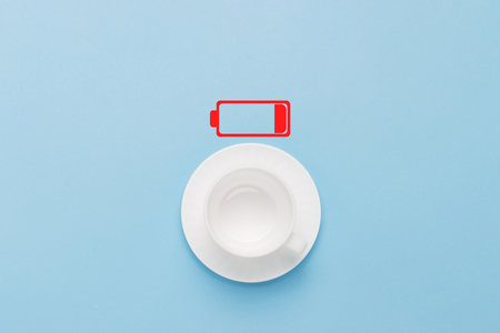 Empty white cup and a discharged battery on a blue background. Concept recharge, time for coffee....