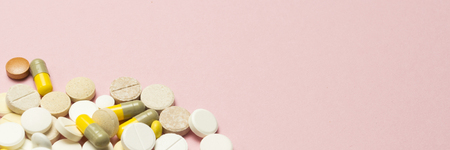Pills of different sizes and colors on a light pink background. Concept of the pharmaceutical industry, daily vitamins and minerals for women. Pregnancy, menopause. Banner.の写真素材