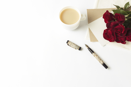 Bouquet of red roses and an envelope with a note, a white cup of coffee with milk, a fountain pen on a white background. Concept of a romantic gift for a loved one. Wedding themes.の写真素材
