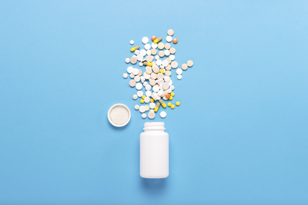 White bottle and multi-colored pills on a blue background. Concept of pharmaceuticals, medicine, drugs and treatment for diseases. Flat lay, top view.の写真素材