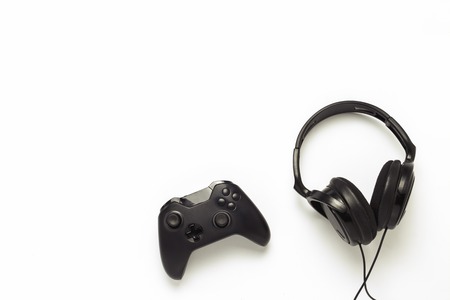 Black headphones and a gamepad on a white isolated background. Concept of the game on the console or...