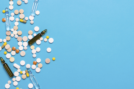 Pills of different colors and ampoules with medicine on a blue background. Concept of the pharmaceutical industry, medicine, treatment and recovery after illness. Flat lay, top view.の写真素材