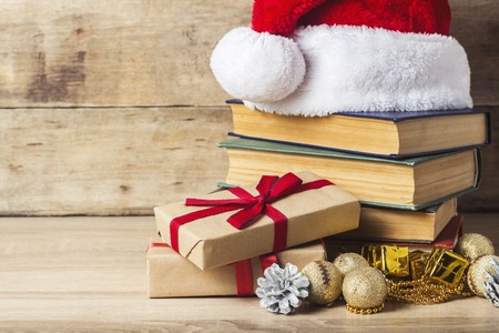 A stack of books, Santa Claus's cap, an alarm clock, cones, Christmas-tree decorations, gift boxes on a wooden background. Concept of New Year and Merry Christmasの写真素材