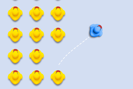 Group of yellow ducklings moves in line direction, but one blue duck swims in another direction. Blue background. The concept of innovative and creative business solutions. Flat lay, top viewの写真素材