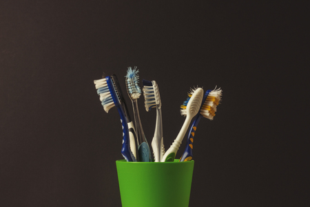 Many toothbrushes in a plastic cup on a black background. The concept of changing toothbrushes, oral hygiene, dentistry. Big and friendly familyの写真素材