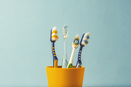 Many toothbrushes in a plastic cup on a blue background. The concept of changing toothbrushes, oral hygiene, dentistry. Big and friendly familyの写真素材