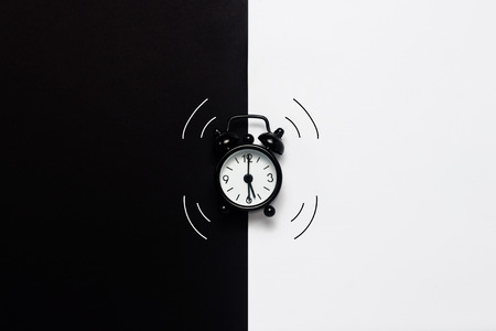 Black ringing alarm clock on black and white background. Concept day and nightの写真素材