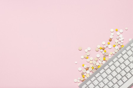 Keyboard and pills on pink background. The concept of ordering and buying medicines, vitamins and pills on the Internet, an online store. Flat lay, top viewの写真素材