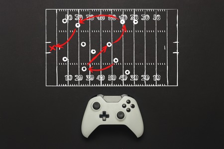 White gamepad on a black background. Added a soccer field scheme. Tactics of the game. Concept game of American football on the console, computer games. Flat lay, top viewの写真素材