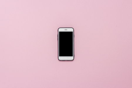 White mobile phone in a black case on an isolated pink background. Flat lay, top viewの写真素材
