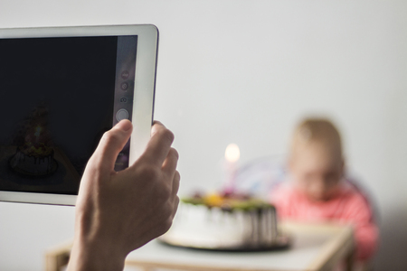 Mom takes a picture of a child with a birthday cake. The concept of the first birthday, one year, a party in honor of the child's birthday, social networks, memoryの写真素材