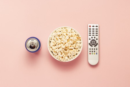 A bowl of popcorn, a TV remote, a jar of drink on a pink background. The concept of watching TV, film, TV series, sports, shows. Flat lay, top viewの写真素材