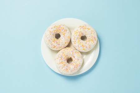 Donuts on a white plate on a blue background. The concept of fast food, morning coffee, breakfast. Minimalism. Flat lay, top viewの写真素材