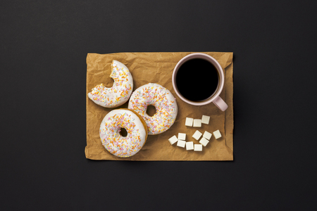 Delicious, sweet, fresh donuts, a cup of coffee, a paper packaging bag for takeaway food, black background. Concept of breakfast, fast food, coffee shop, bakery, lunch. Minimalism. Flat lay, top viewの写真素材